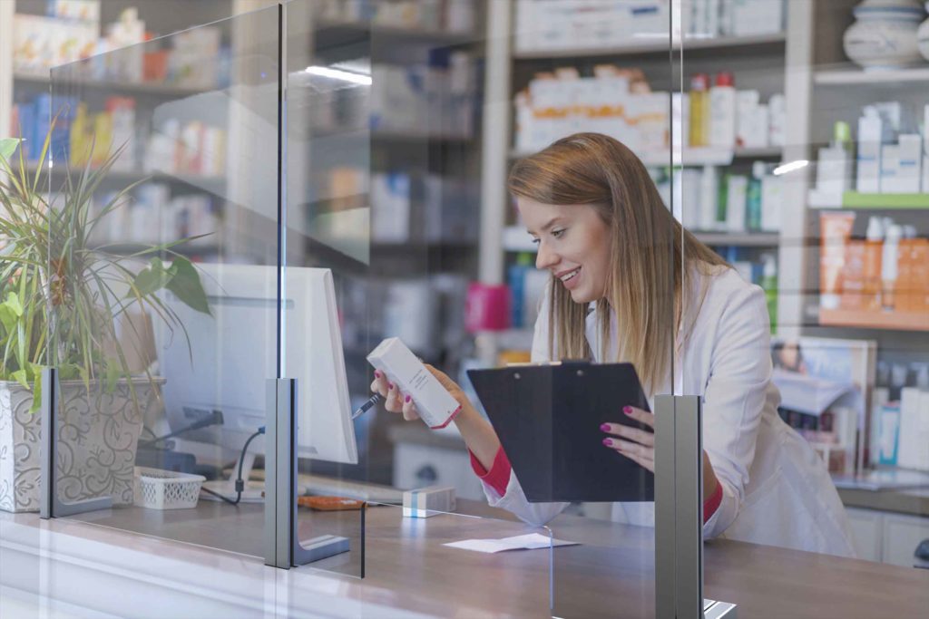 woman holding medicine behind sneeze safety glass